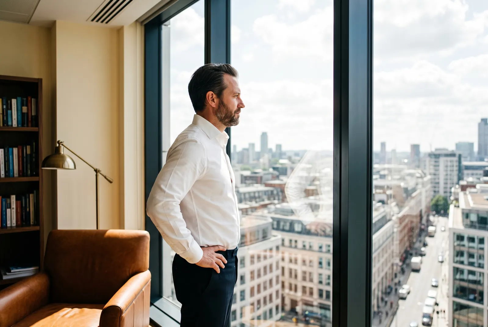 A man in a white shirt looks out over a city skyline from a high-rise window