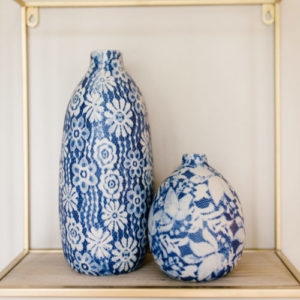 Two blue vases on a wood shelf under a gold rack