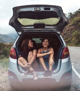 Girls sitting in trunk of car on the side of a road through the mountains