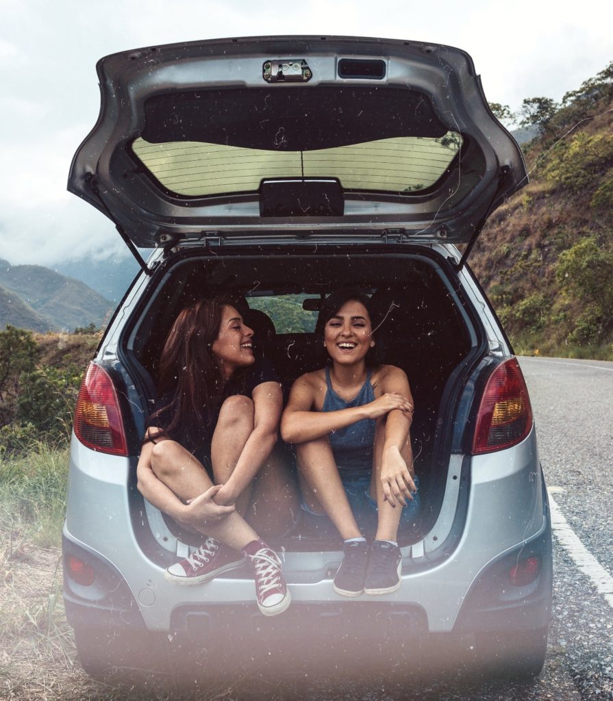 Girls sitting in trunk of car on the side of a road through the mountains