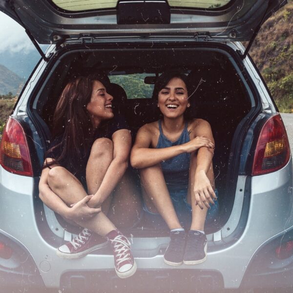 Girls sitting in trunk of car on the side of a road through the mountains