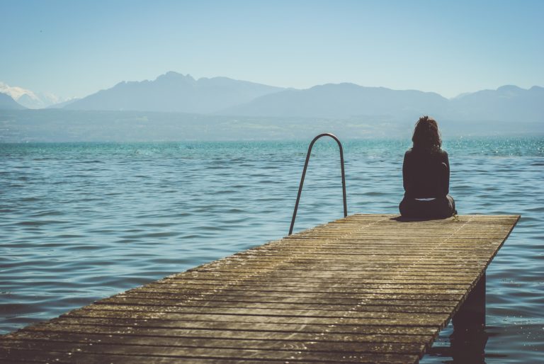 Woman sitting at the end of a dock looking off into the distance